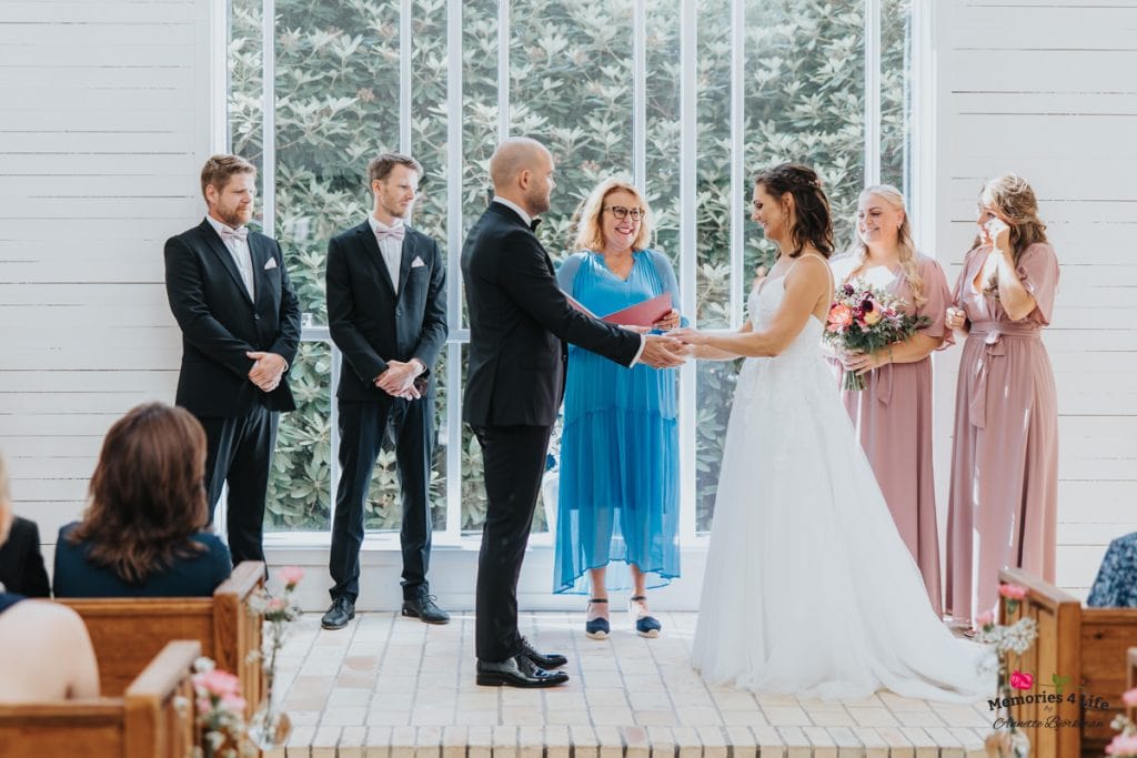 Bröllopsceremoni med brud och brudgum i vacker kyrka, omgiven av bröllopsfölje och gäster.