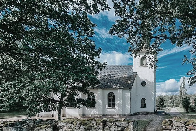 Norumkyrka i vaker miljö omgiven av gröna träd och blå himmel