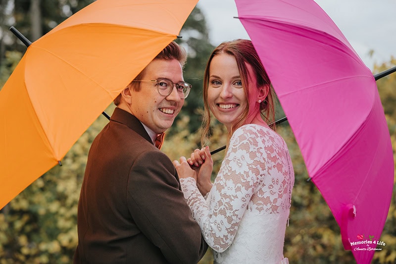 Leende Brudpar under orange och rosa paraply