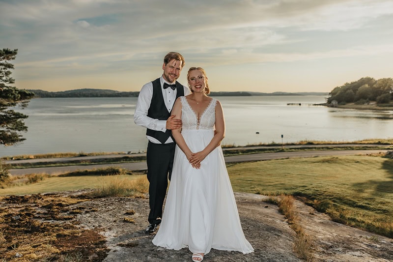 Brudpar som står med vattnet bakom sig i golden hour.