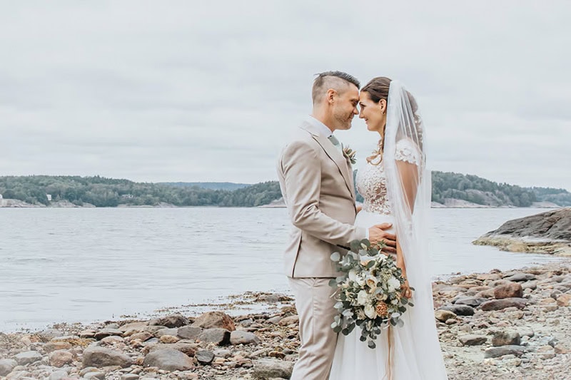 Brudpar står näsa mot näsa och myser på stranden